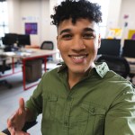 Biracial man smiling looking at the camera on smartphone during a video call at office. Business, technology and office concept